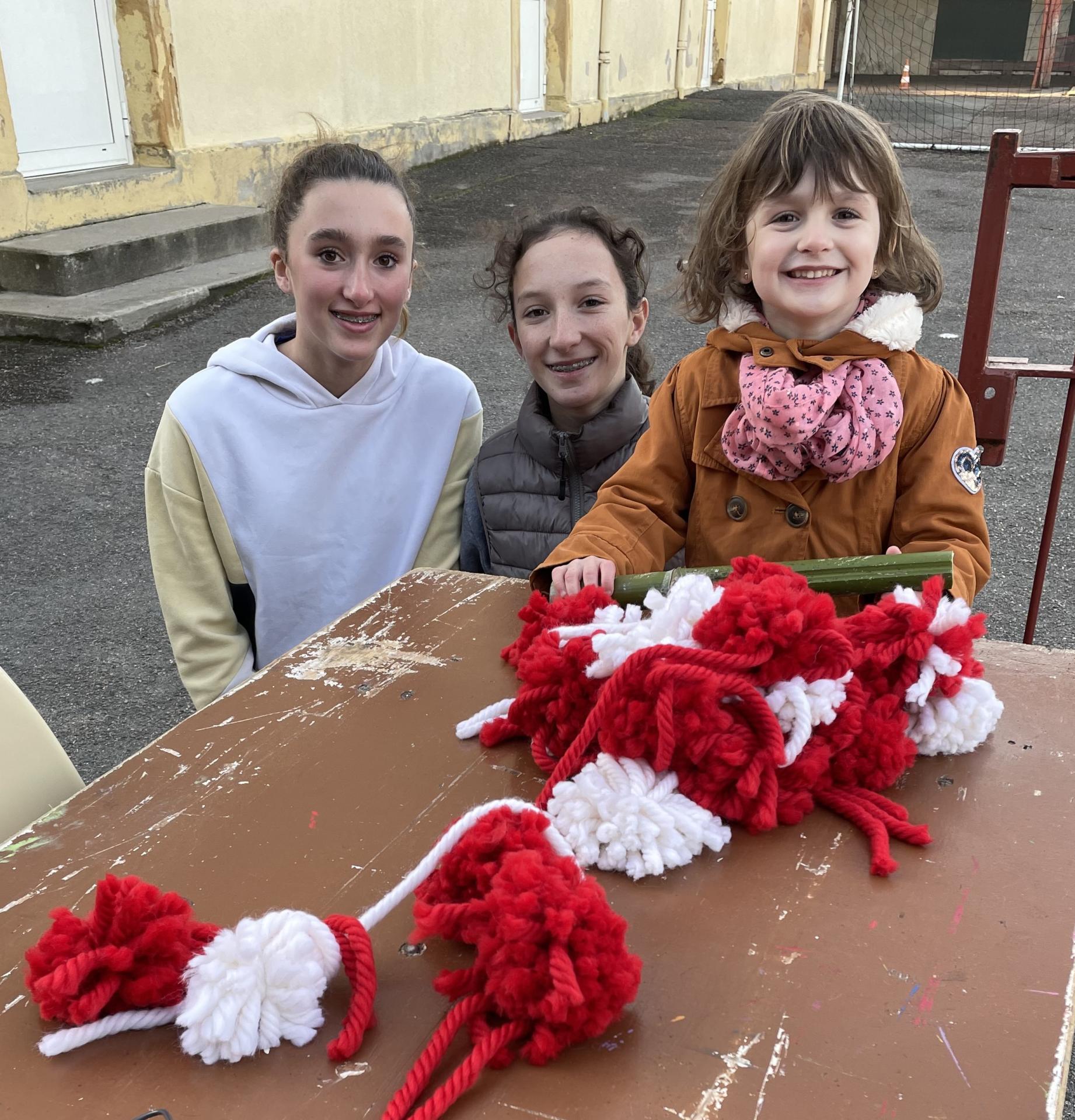 trois enfants assises devant pompons rouges et blancs